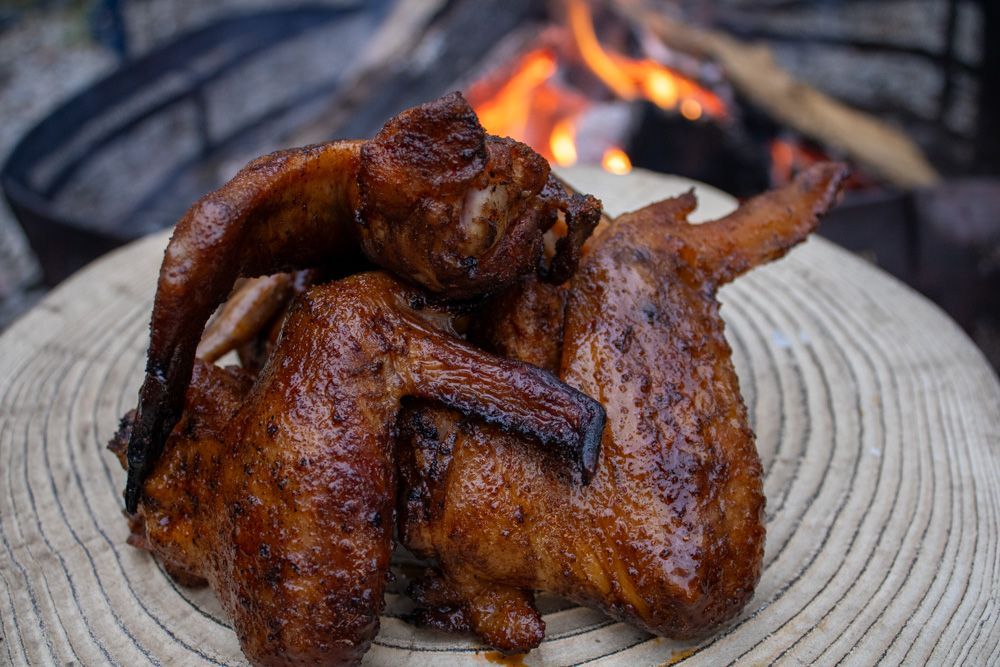 A plate of chicken wings on a wooden cutting board with a fire in the background.