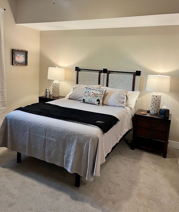 Bedroom with bed, nightstands, lamps, and a small framed picture. Light neutral colors.