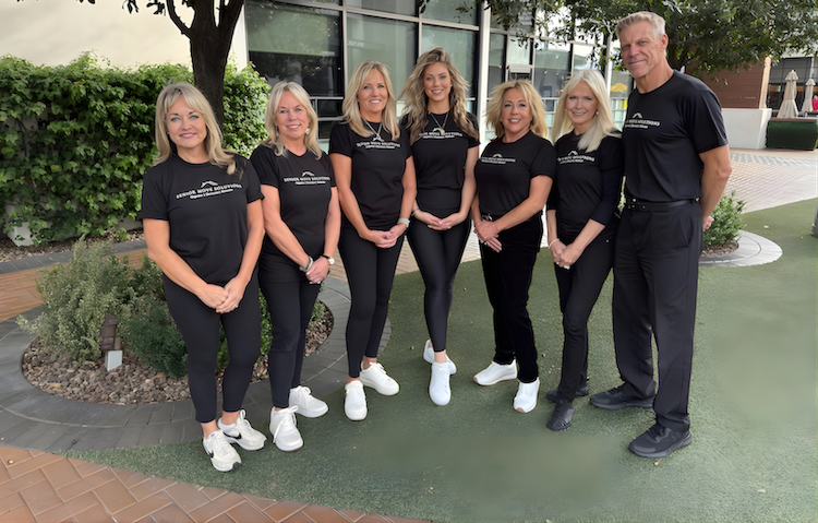 Seven people in black athletic wear pose outside.