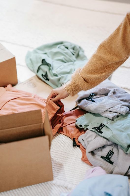 Person sorting colorful shirts into boxes on a white surface.