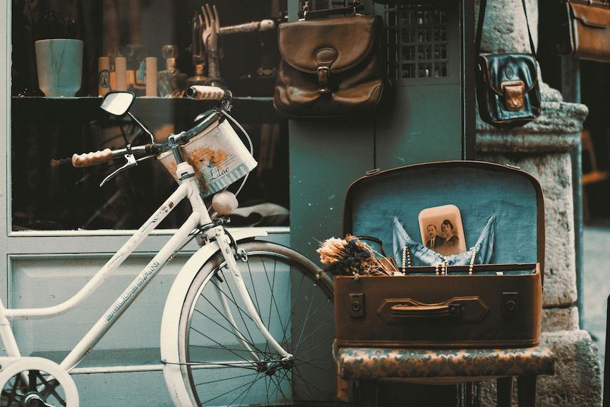 White bicycle parked next to an open suitcase filled with items; antique shop backdrop.