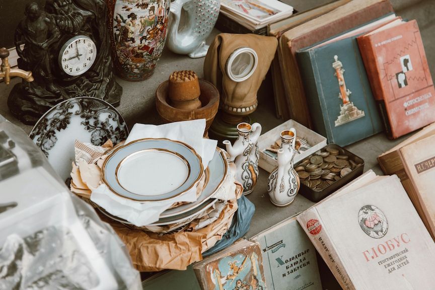Assorted vintage items on a table, including books, plates, clock, vase, and gas mask.