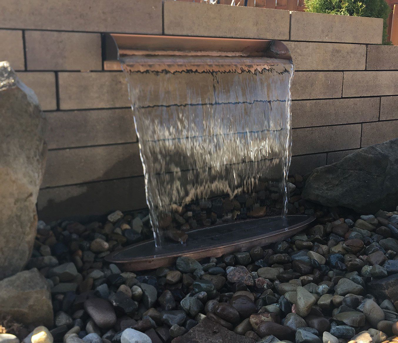 Spillway water feature with scupper surrounded by rocks set into paver block wall