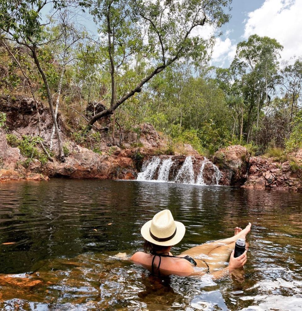 A woman is laying in a pond with a waterfall in the background.
