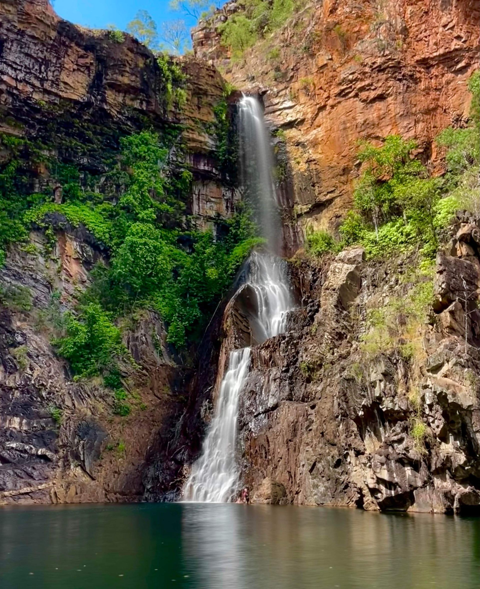 A waterfall is coming down a cliff into a lake surrounded by trees.