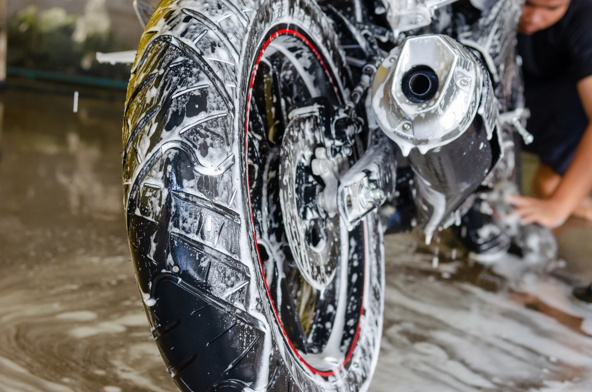 Una motocicletta viene lavata, con la ruota posteriore e lo scarico ricoperti di schiuma in un garage bagnato.