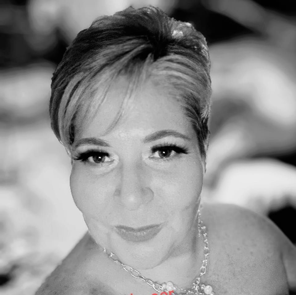 A woman with short hair is wearing a necklace and smiling in a black and white photo.