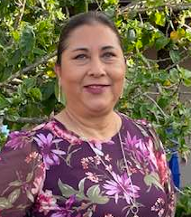 Woman with glasses, smiling, wearing a black and white floral print top, against a grey background. Dion Brady
