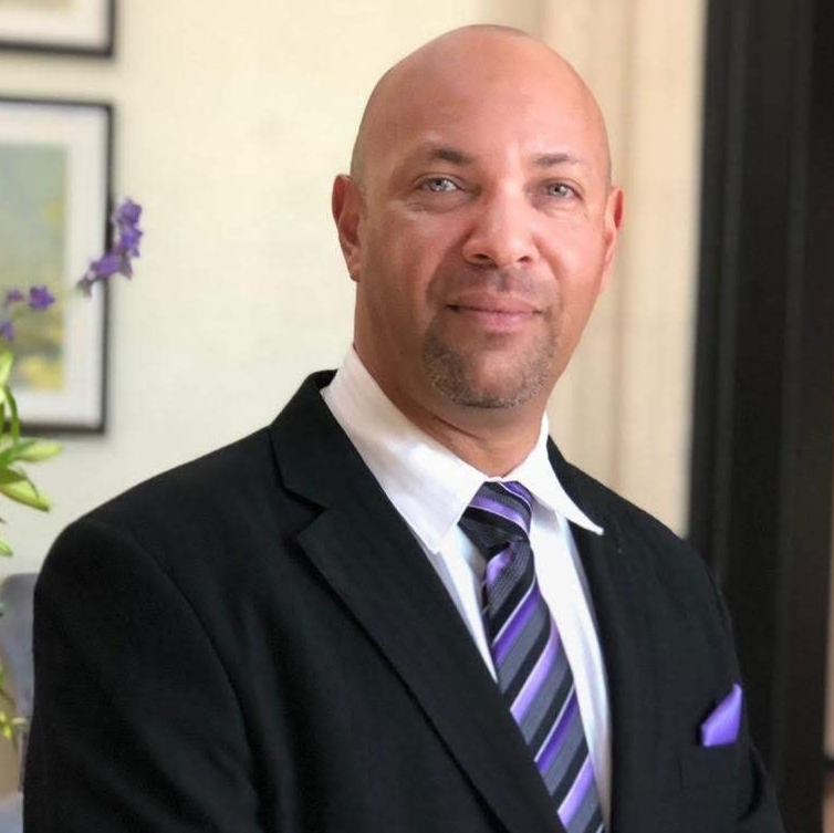 A bald man wearing a black suit and purple tie