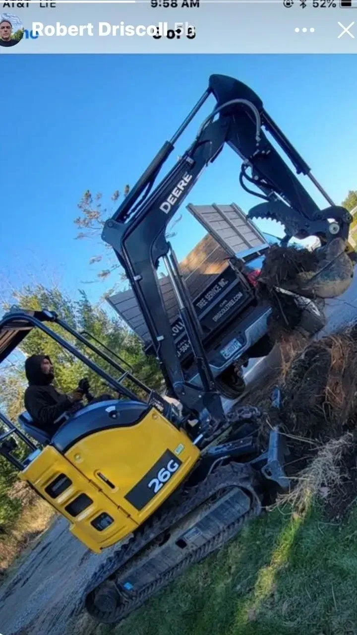 Excavator on a hill, removing debris. Yellow and black machine with operator, sunny outdoors.