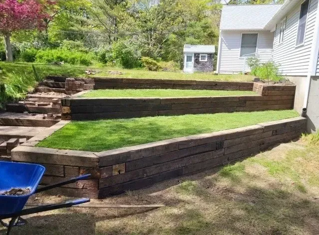 A tiered backyard with railroad tie retaining walls, green grass, and stairs leading up to a house.