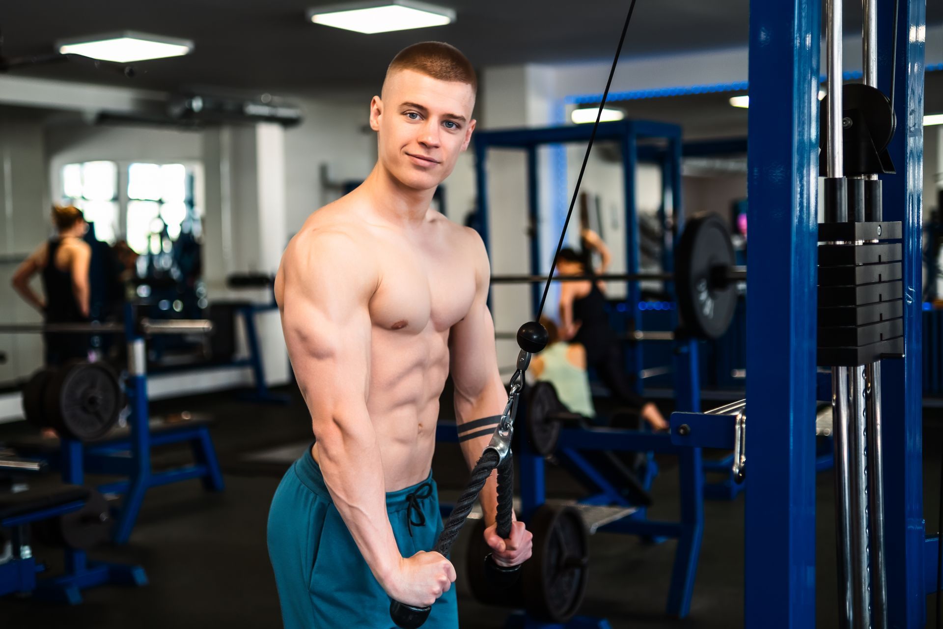 Homem musculoso treina tríceps em máquina de cabo na academia, destacando definição e confiança.