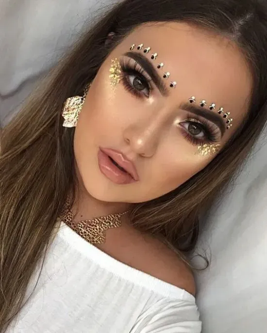 A close up of a woman 's face with makeup and rhinestones on her eyebrows.