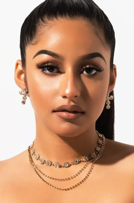 A woman with long eyelash extensions is wearing a choker necklace and earrings.