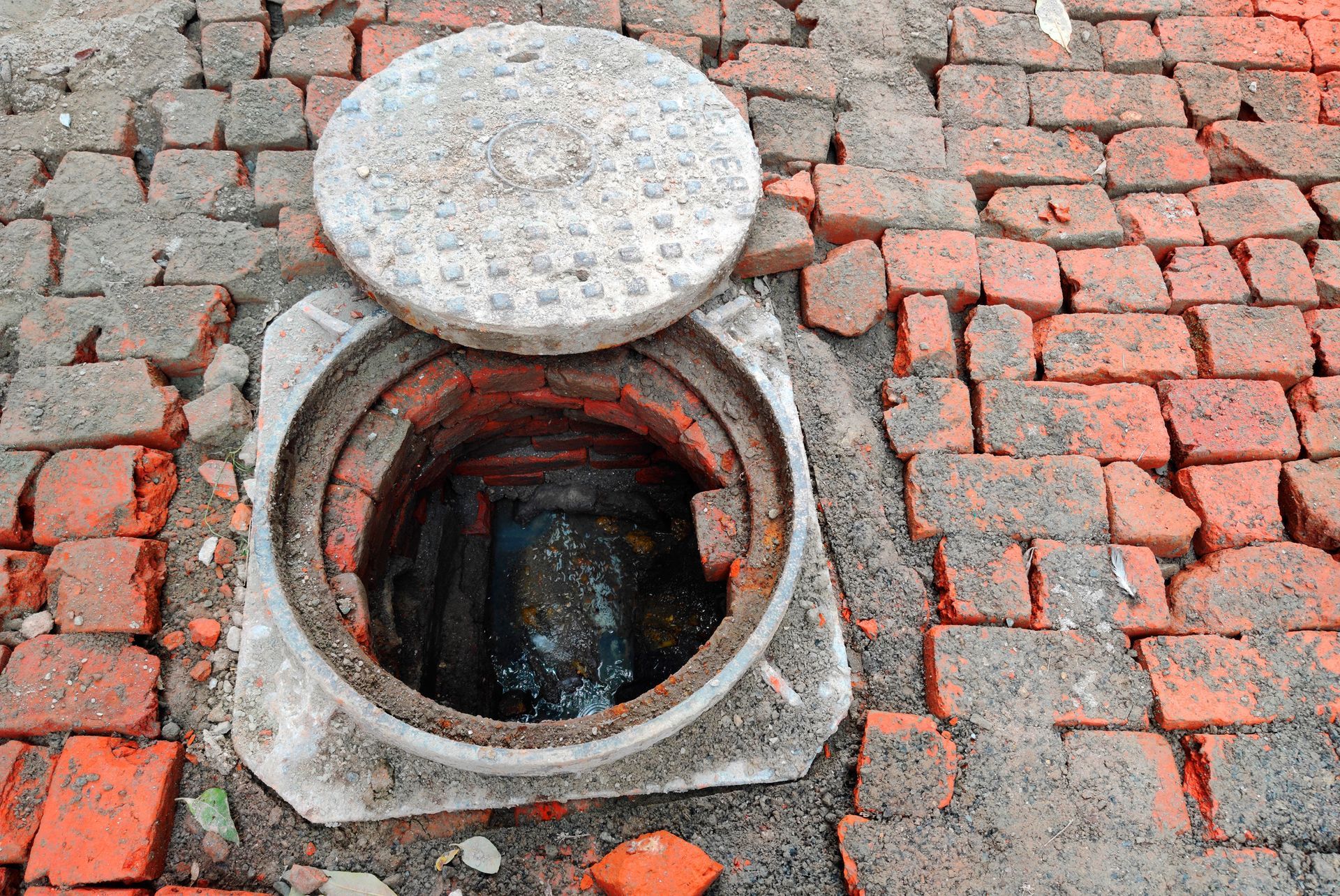 A manhole cover is open on a brick sidewalk.