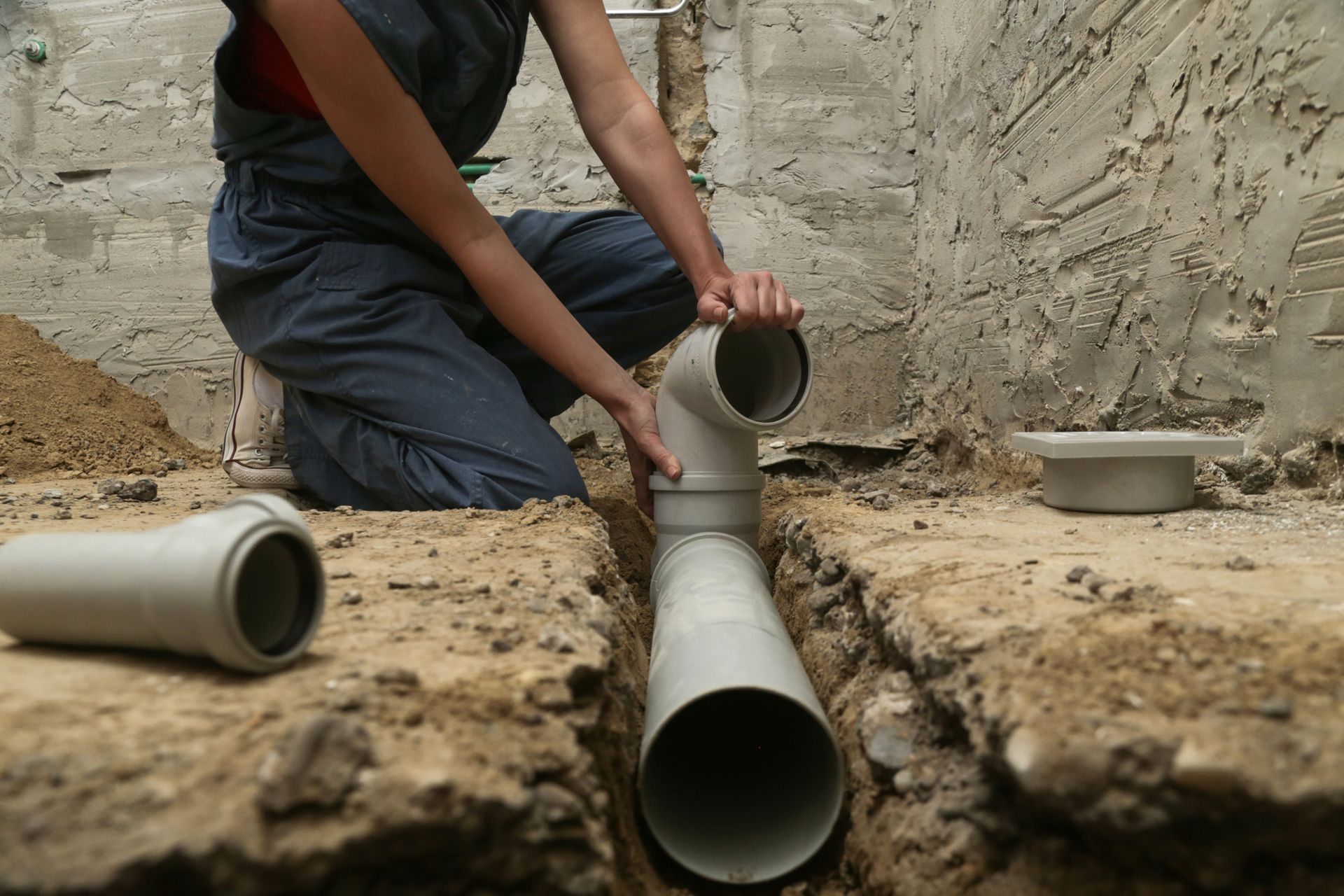 A woman is kneeling down in the dirt holding a pipe