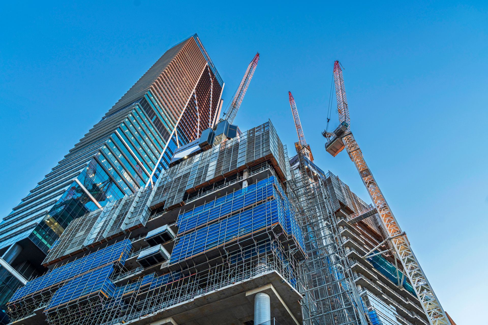 Looking up at a tall building under construction with cranes.