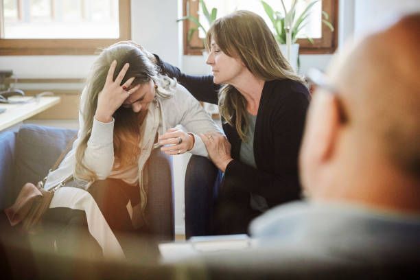 A woman is comforting another woman who is sitting on a couch.