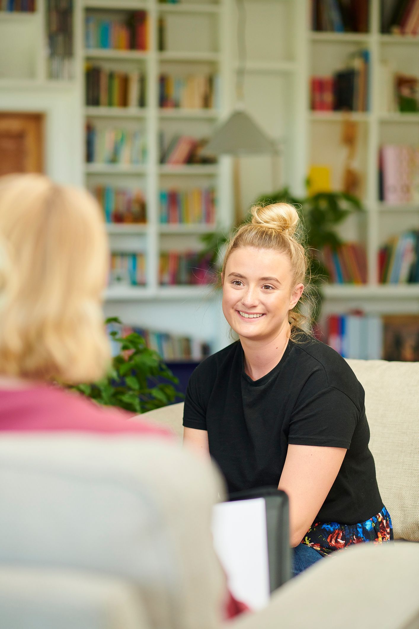 A woman is sitting on a couch talking to another woman.