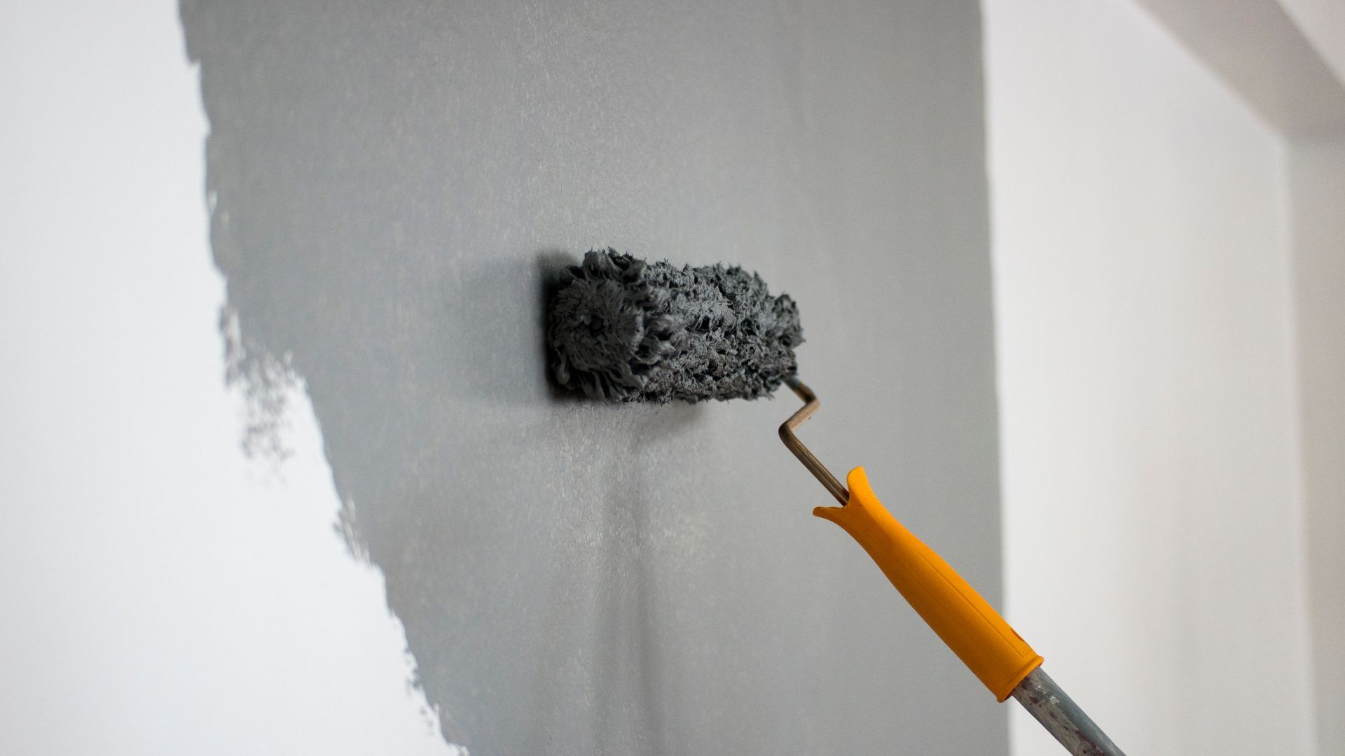 A person is painting a wall with a paint roller.