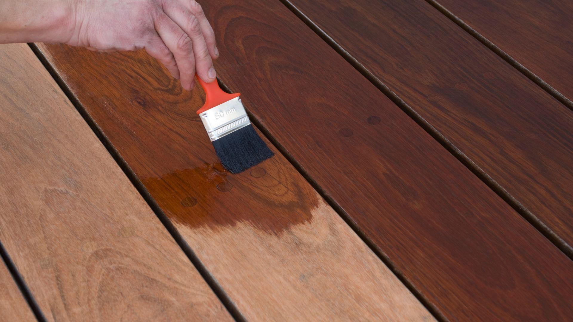 A person is painting a wooden deck with a brush.