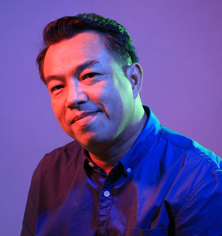 Man with headphones dances joyfully, holding phone, lit by pink and blue light.