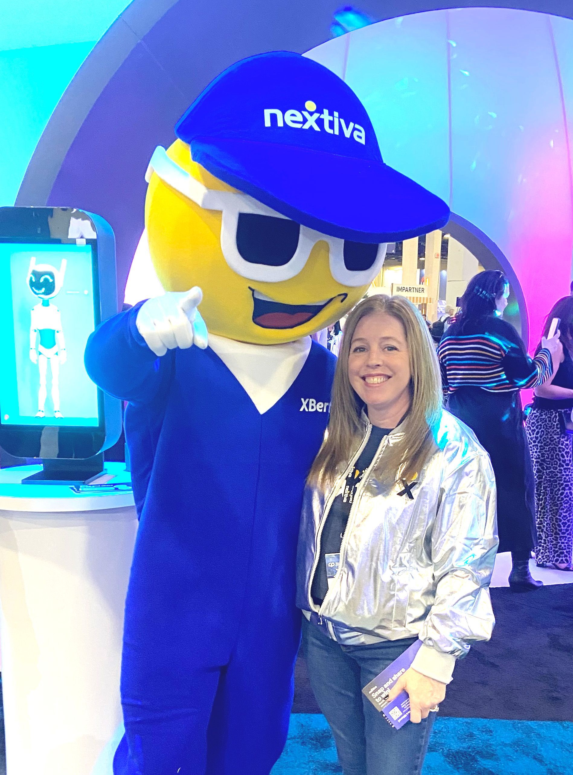 Young Black woman smiles, points up, bathed in pink and purple light. Wearing glasses and a red jacket.