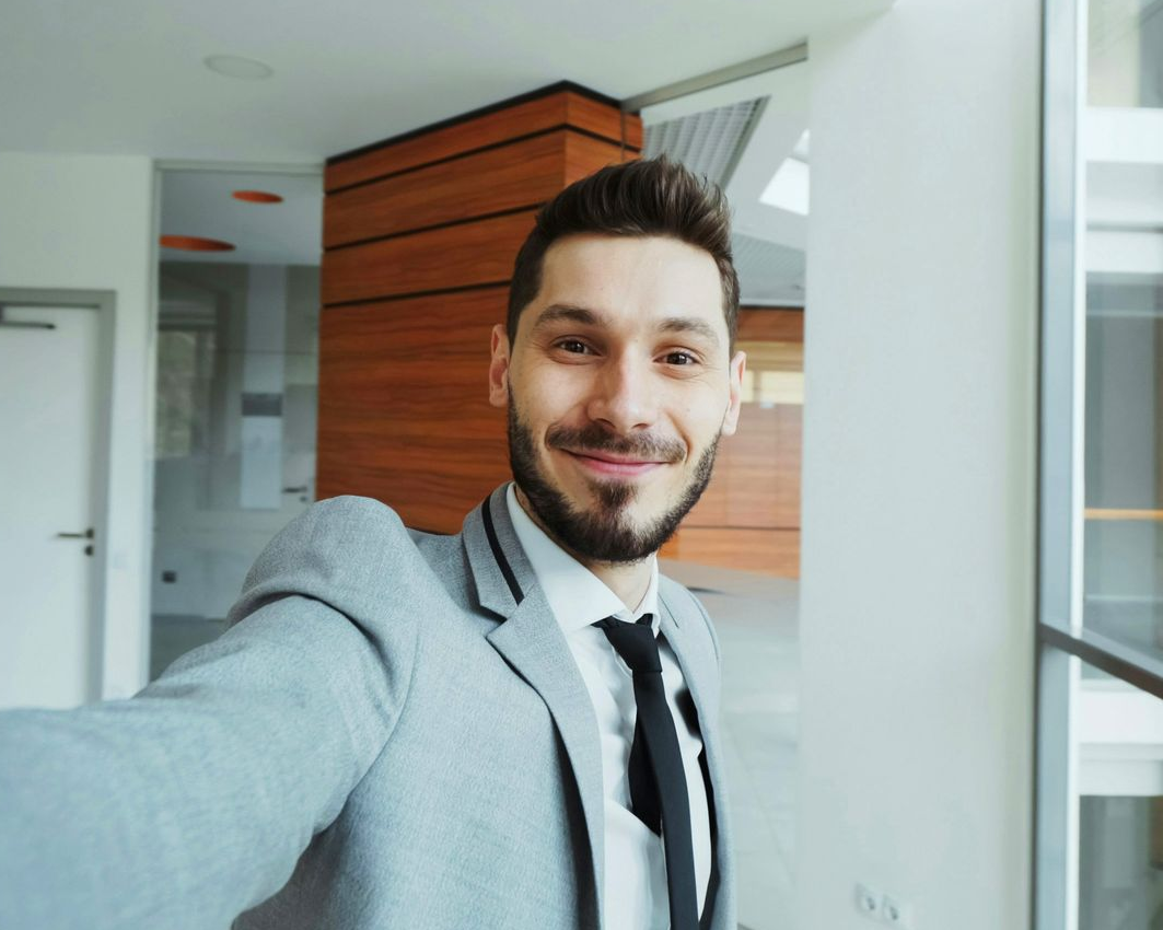 Woman with long brown hair smiles and points right, against blue and pink backdrop.