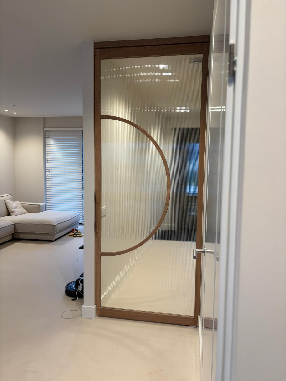 Een moderne deur met houten frame, geribbeld glas en een opvallend halfrond ontwerp, geplaatst in een eigentijdse woonruimte.