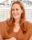 A woman with red hair is wearing sunglasses and smiling.