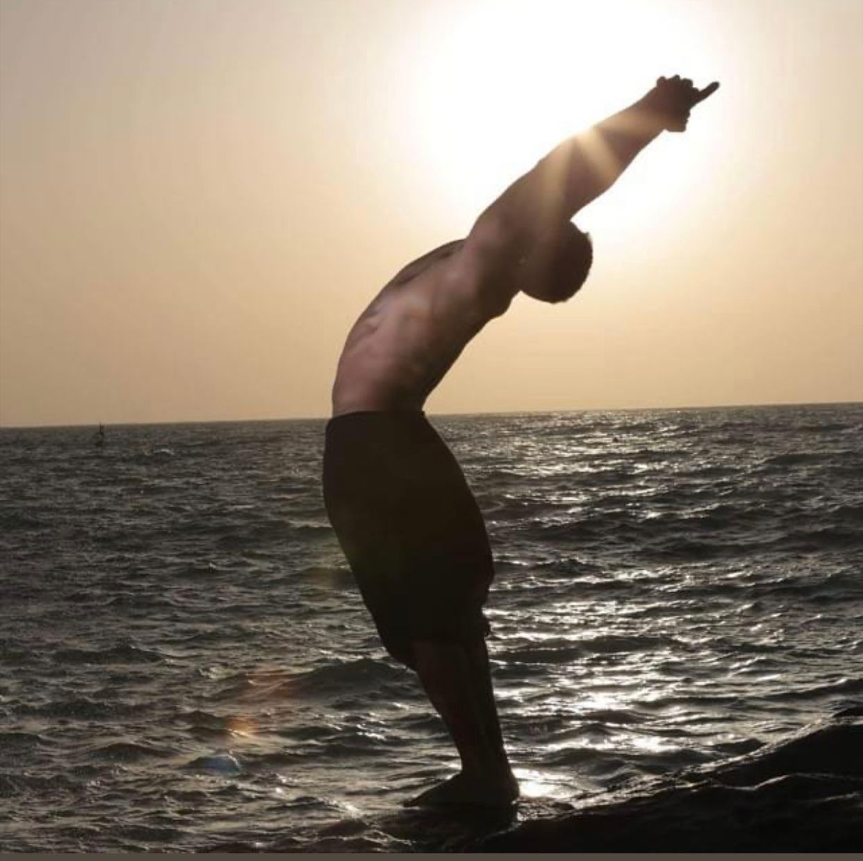 A shirtless man is doing a handstand in the ocean
