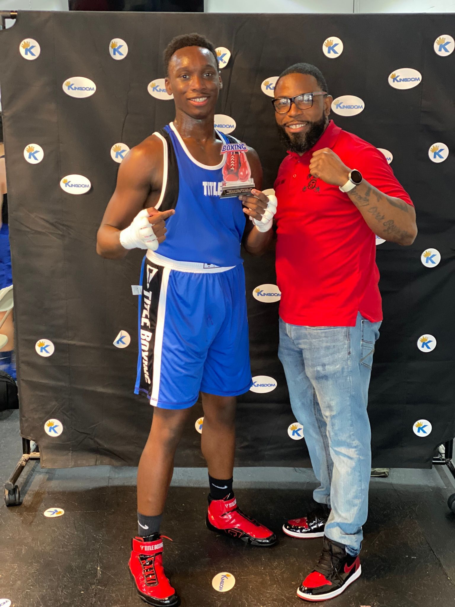A man in a red shirt is standing next to a boxer holding a trophy.