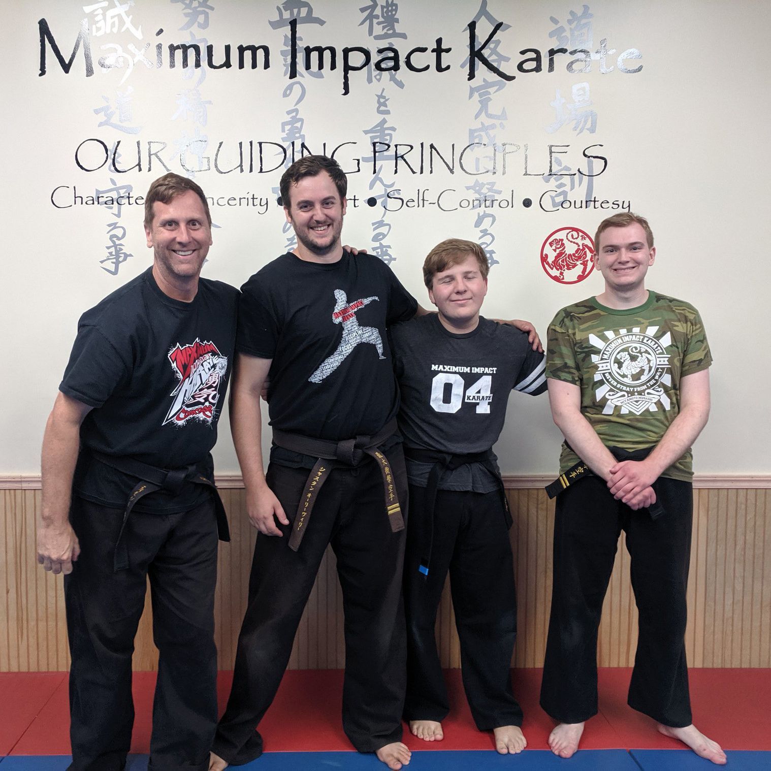 Four men are posing for a picture in front of a wall that says maximum impact karate