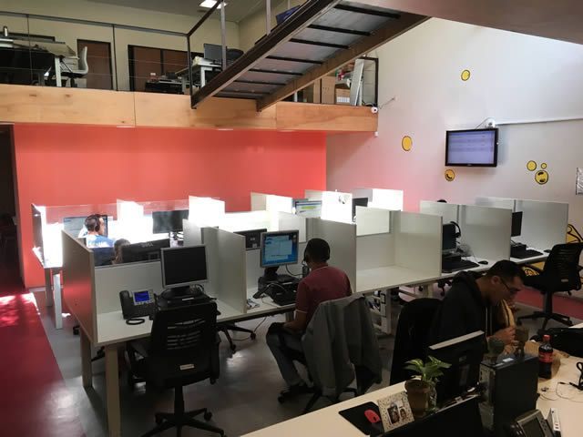 Espacio de trabajo de oficina con filas de cubículos, personas trabajando en computadoras y un nivel de entrepiso.