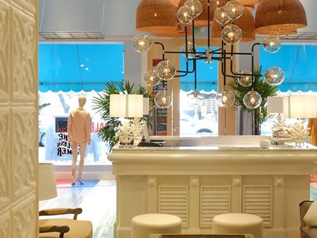 Interior de una tienda luminosa con un mostrador blanco, una lámpara de araña y un maniquí en el escaparate.