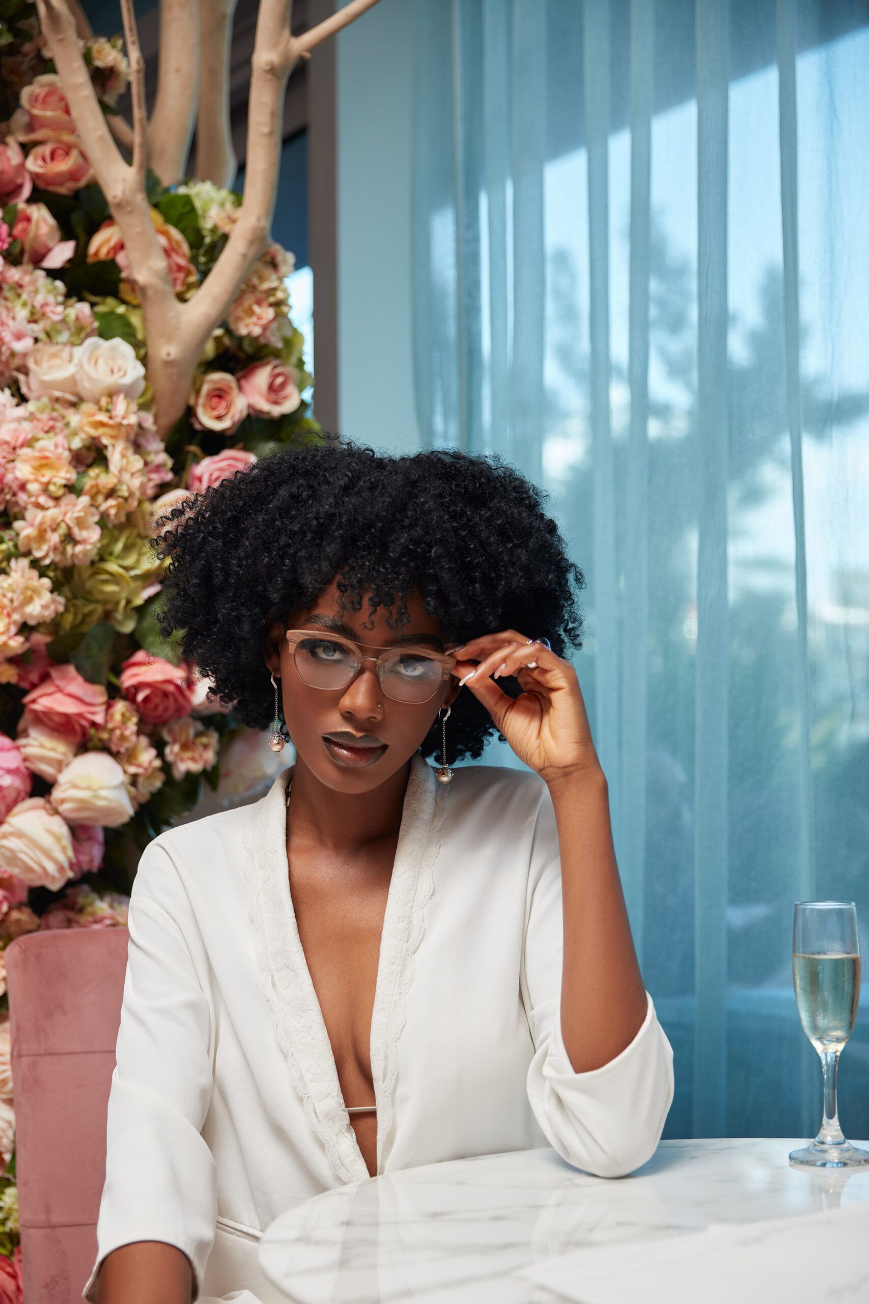 A woman wearing glasses is sitting at a table with a glass of wine.