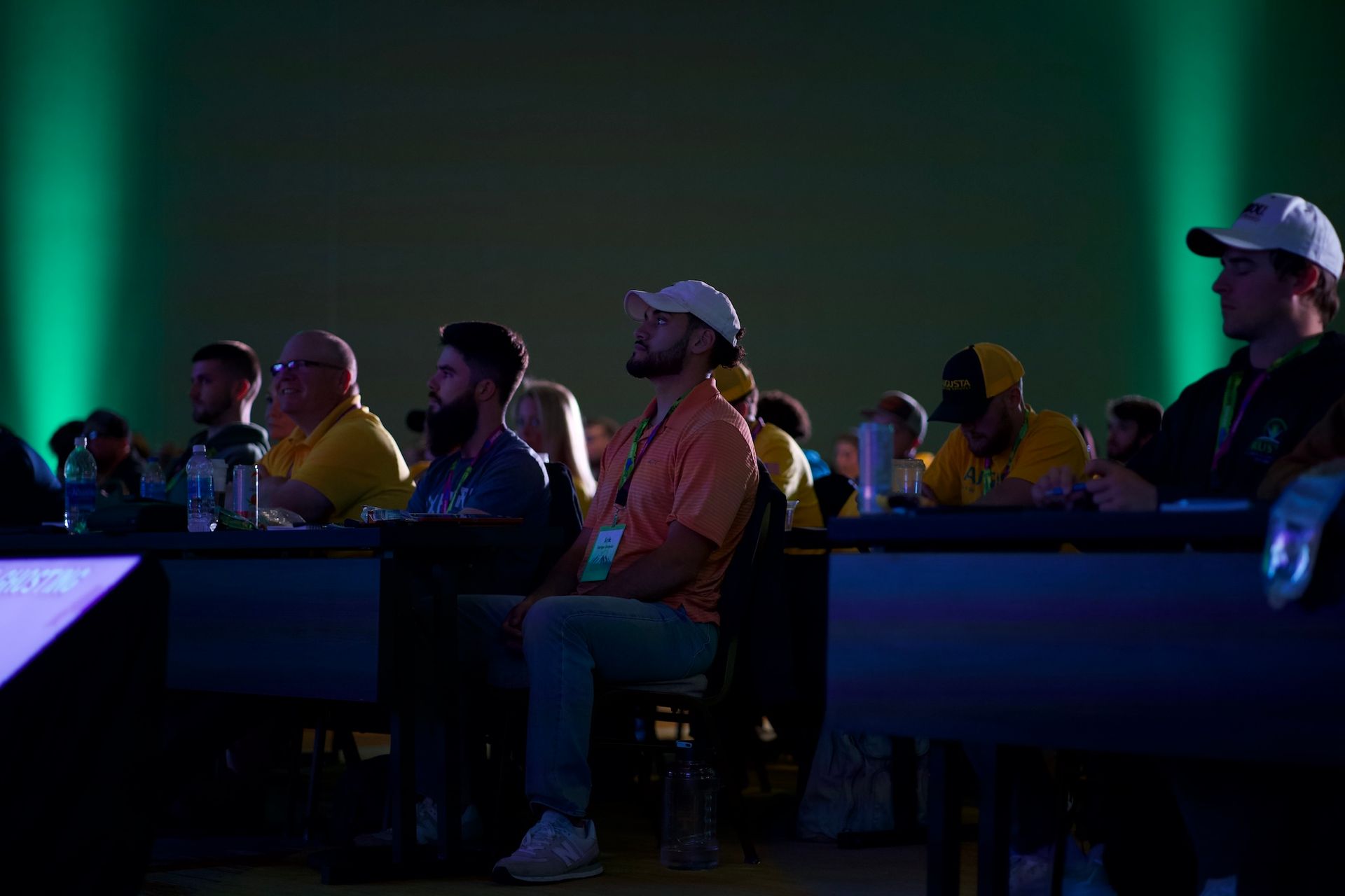 A group of people are sitting at tables in a dark room watching a presentation.