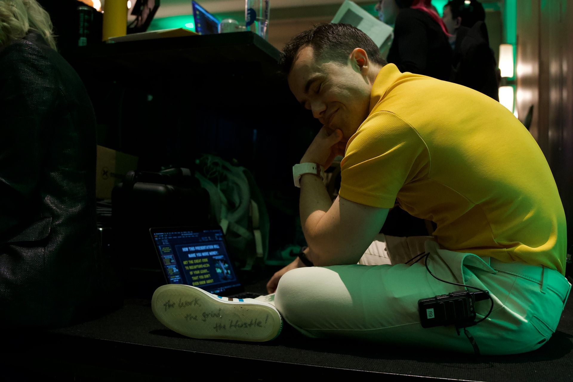 A man in a yellow shirt is sitting on the floor using a laptop computer.