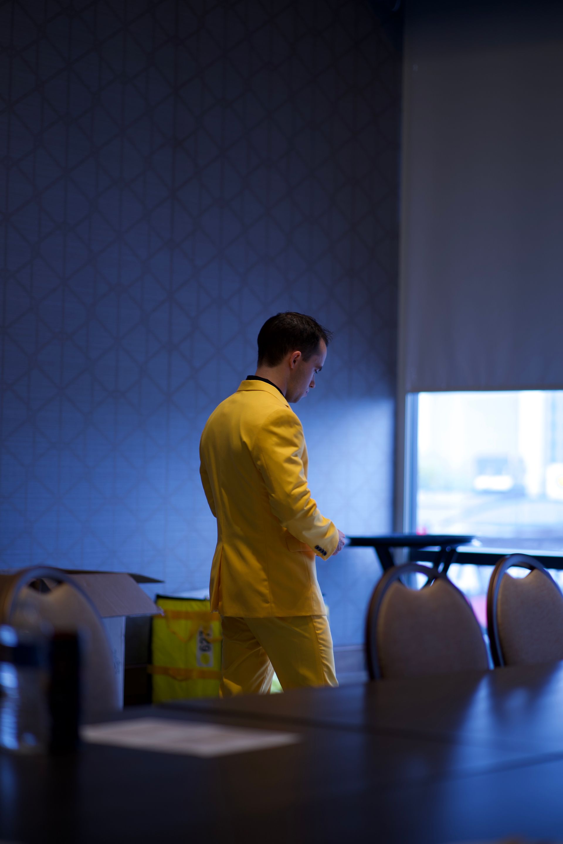 A man in a yellow suit is standing in front of a conference table.