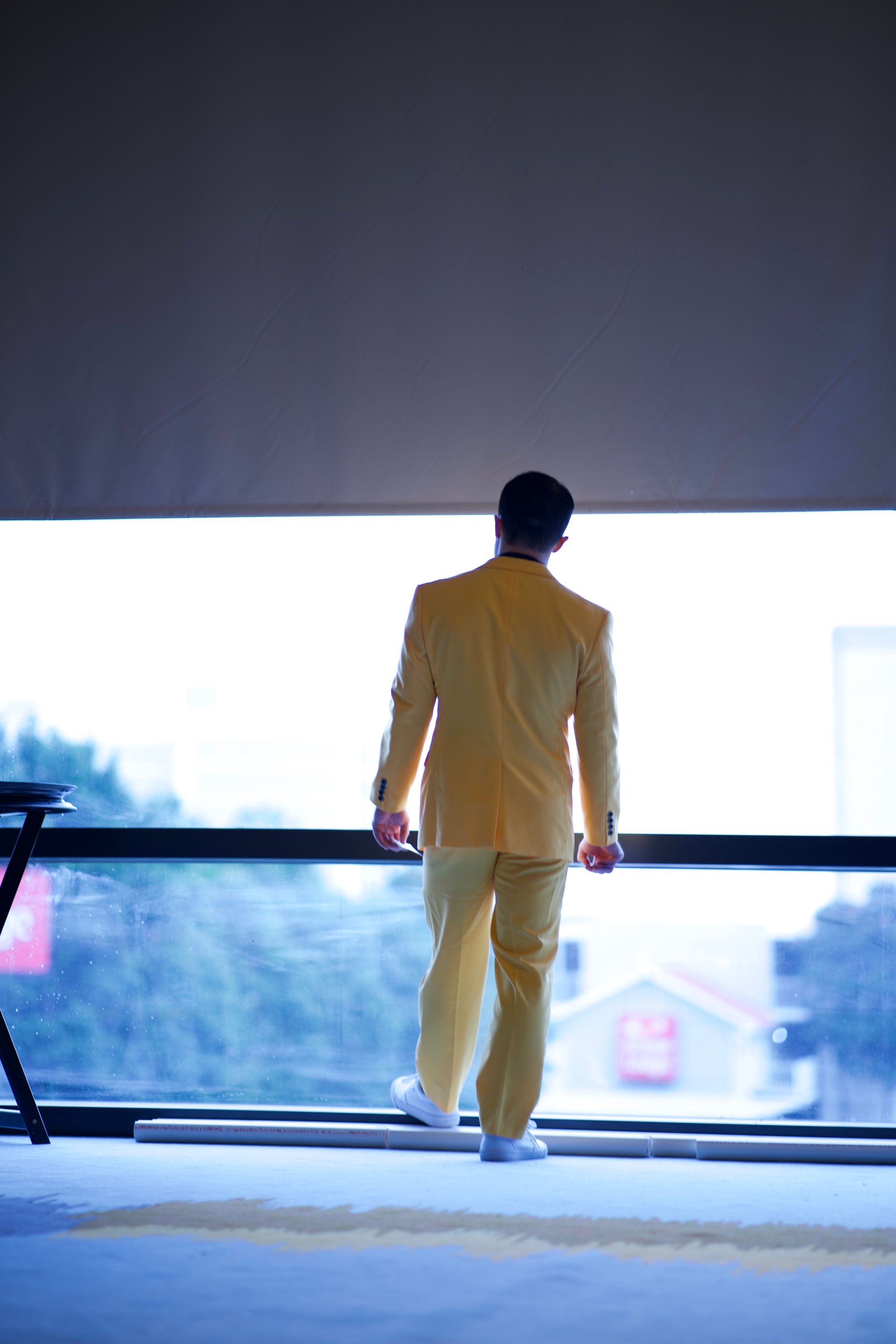 A man in a yellow suit is standing on a balcony looking out a window.