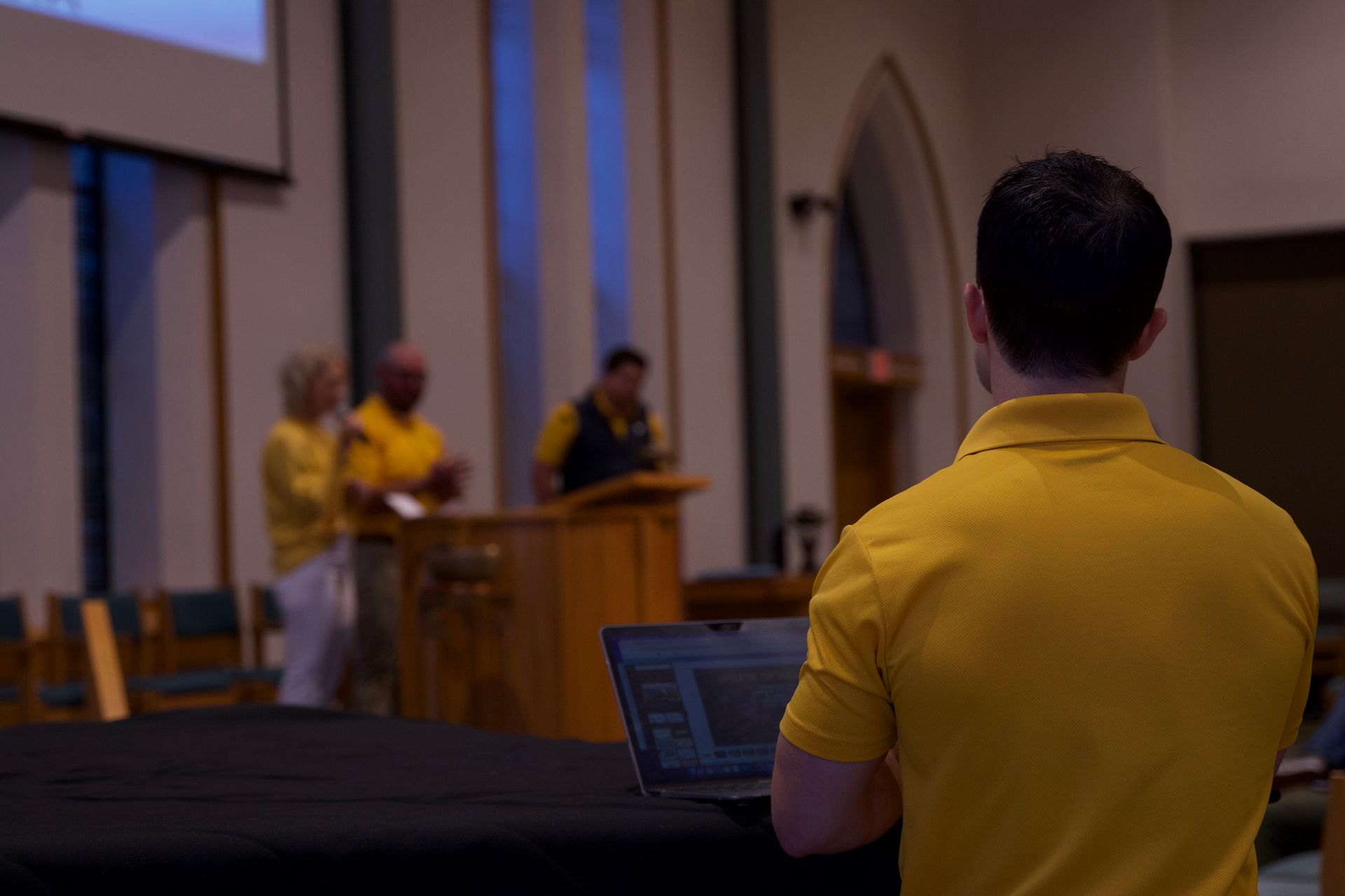 A man in a yellow shirt is standing in front of a laptop computer.