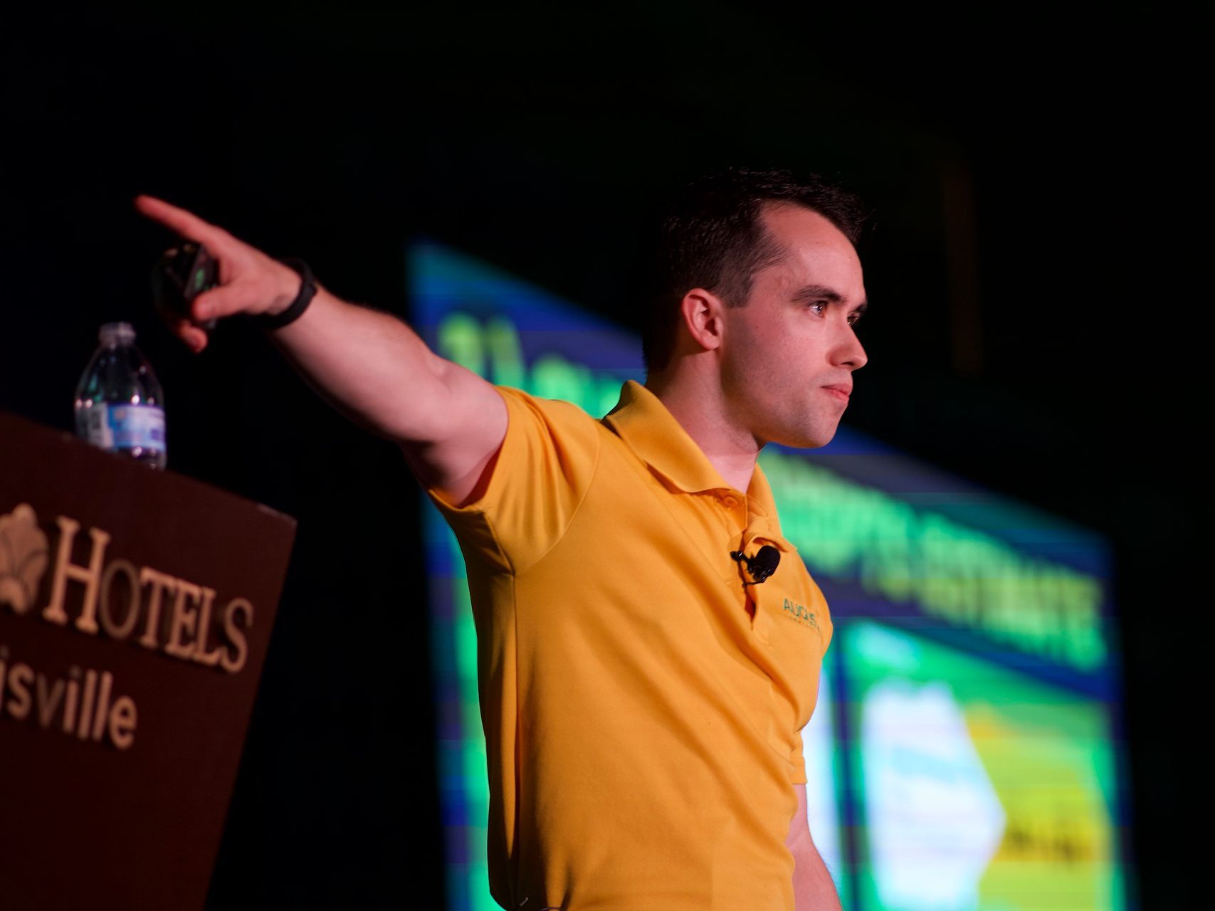 Mike Andes in a yellow shirt is standing in front of a podium that says hotels