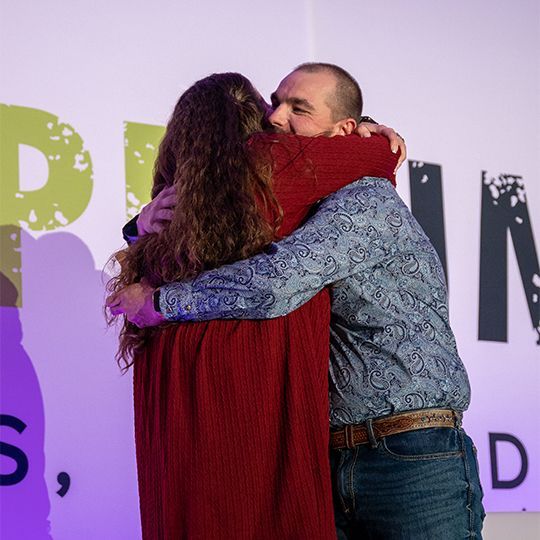 A man and a woman are hugging in front of a sign that says p.i.n.