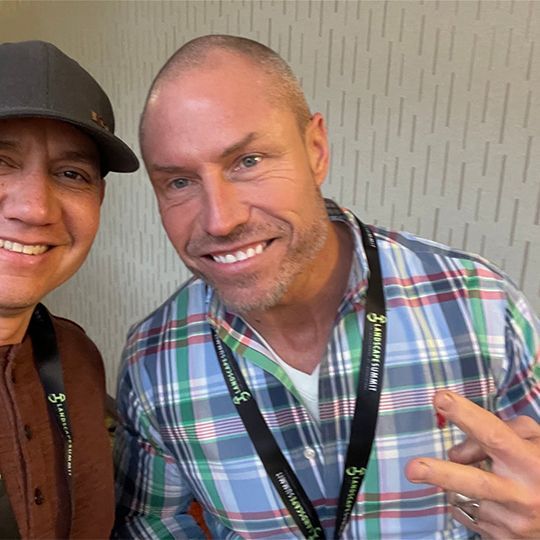 Two men are posing for a picture and one has a lanyard around his neck that says ' allianz ' on it