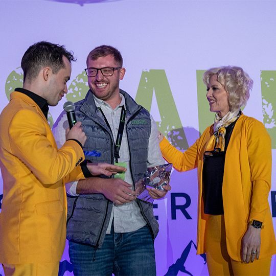 A man in a yellow suit is holding a microphone and talking to two other people.