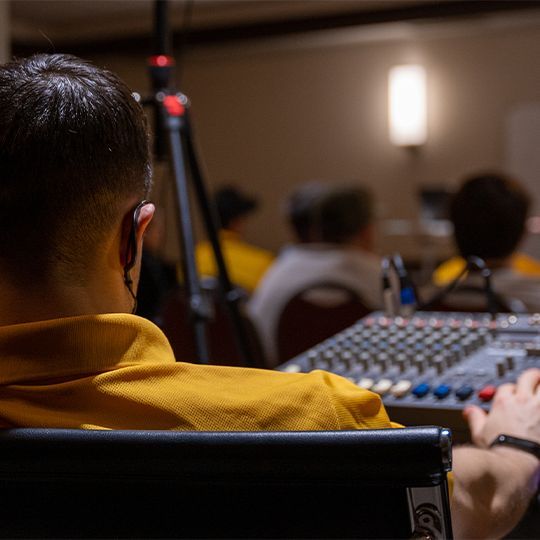 A man in a yellow shirt is sitting in front of a mixer