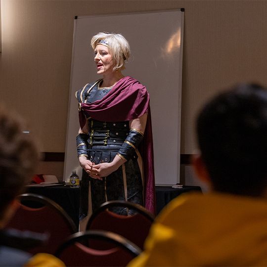 A woman in a costume stands in front of a group of people