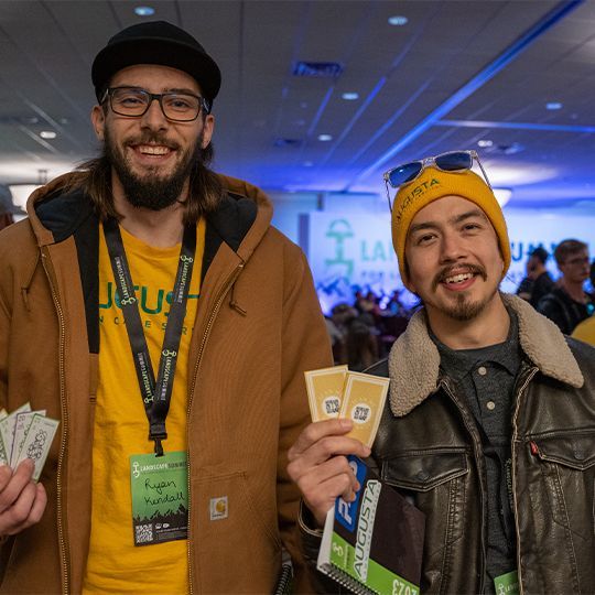 Two men are posing for a picture and one is wearing a yellow hat