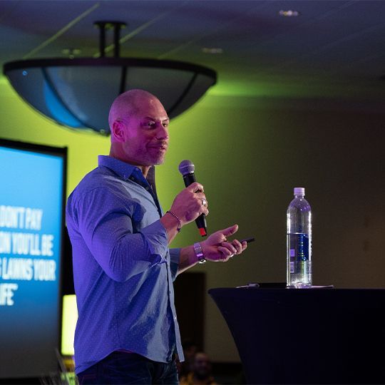 Kory Ballard is holding a microphone in front of a sign that says 