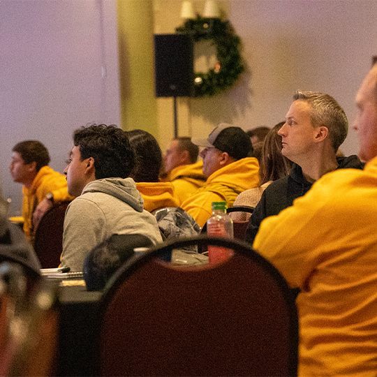 A group of people in yellow shirts are sitting in a room